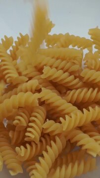 Macro close up shot of dry yellow fusilli pasta spirals tumbling down into a white container, Italian cuisine and food preparation video.