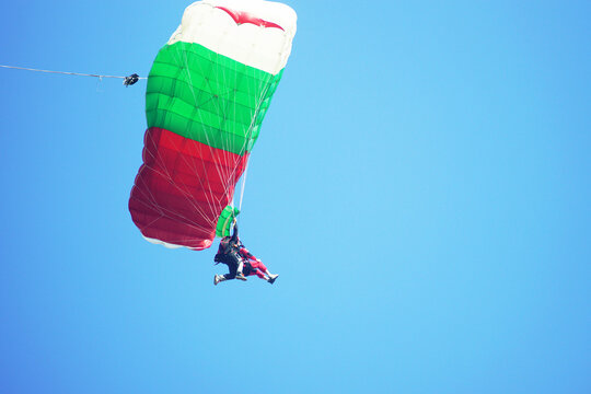 Close-up of skydivers pair steering bright tricolor canopy during descent. Captures active parachute control, first-time skydiving, thrilling extreme adventure experience, and personal challenge.