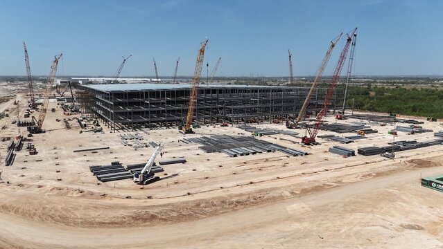 Aerial views of commercial building under construction with steel framing, surrounded by tower cranes
