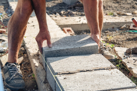 Man laying stone blocks on a construction site during daytime in a rural area