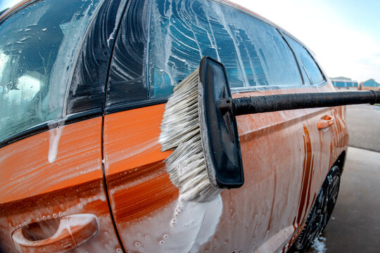 Car washing with a brush on a sunny day near a car wash station