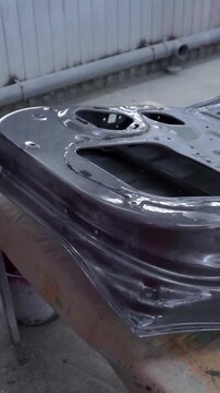 Close-up shot of a car part surface preparation process, with a worker smoothing primer and metal prior to painting.