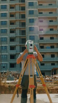 A professional surveyor with a digital total station mounted on a tripod is working at a construction site 