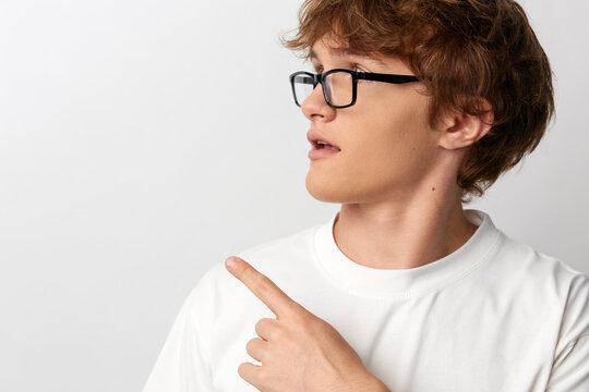 Side profile of young man in glasses and white t-shirt pointing finger toward open copy space, perfect for navigation apps, guided content teasers and directional cues.