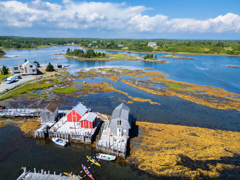 Aerial view of Blue Rocks in Nova Scotia featuring colorful fishing shacks, wooden walkways, boats, and a rocky coastal landscape at low tide