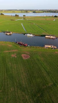 Vertical aerial drone video of houseboats on river, Dutch polder fields, drainage canals, and lake countryside in Warmond, South Holland, Netherlands at golden hour sunset