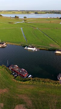 Vertical aerial drone video of houseboats on river, green polder fields, drainage canals, and lake landscape in Warmond, South Holland, Netherlands at golden hour sunset