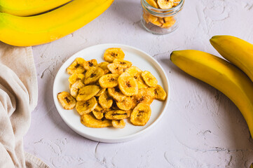 Golden, round, dried banana chips on a plate and fruit on the table © elenarui