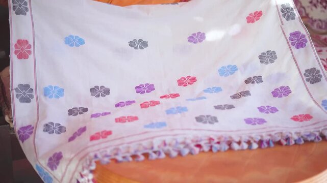 Close view of colorful traditional Assamese fabric with floral patterns and handcrafted textile details in indoor cultural setting, India.