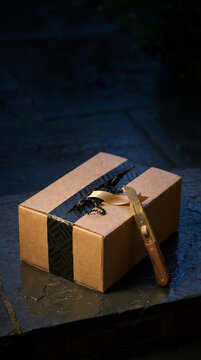 Cardboard gift box with black ribbon and box cutter on wet stone surface. Black Friday retail packaging and holiday shopping. Halloween gift presentation and seasonal commerce