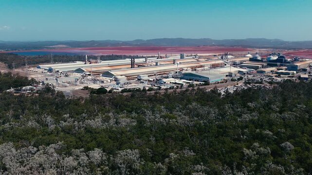 Aerial view of the industrial smelter complex situated near the coastline with surrounding vegetation and red-toned industrial ponds in Boyne Island, QLD, Australia.