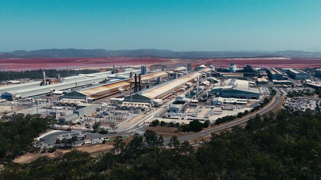 Aerial view of the industrial smelter facility located near the coastline with surrounding vegetation and clear blue sky in Boyne Island, QLD, Australia.