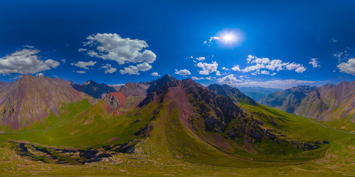 360-degree aerial panorama showcases a mountainous landscape in Kyrgyzstan. Rocky slopes with green vegetation and a river flowing through a valley create a vibrant natural scene.