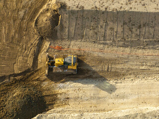 Aerial view of a yellow bulldozer grading earth on a construction site in soft morning light. © Mario