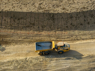 Aerial view of a yellow dump truck driving along a dirt road in a barren construction site. © Mario