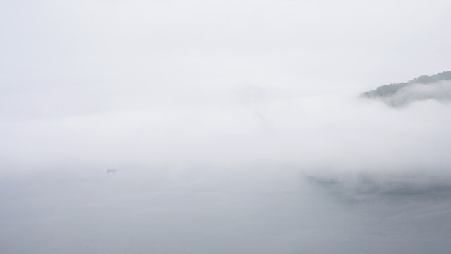 Dense white fog over a body of water with a faint forested hill silhouette, mist on Lake Baikal, Russia. Minimalist misty landscape background. Nature and travel concept