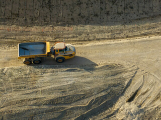 Aerial view of a yellow dump truck driving along a dirt road in a barren construction site. © Mario