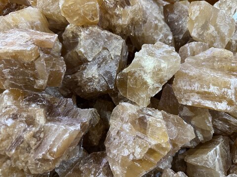 A close-up collection of raw, yellow calcite mineral crystals, honey calcite mineral crystals with natural cleavage planes, glossy crystalline textures, and earthy amber tones, displayed in a pile.