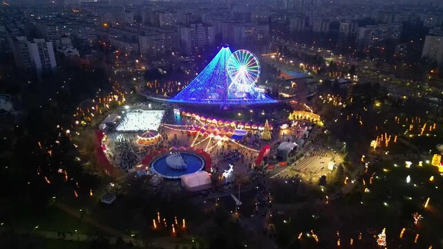 Spectacular drone shot of a crowded winter festival and Christmas market in Bucharest, Romania, illuminated by festive holiday lights and decorations at dusk.	
