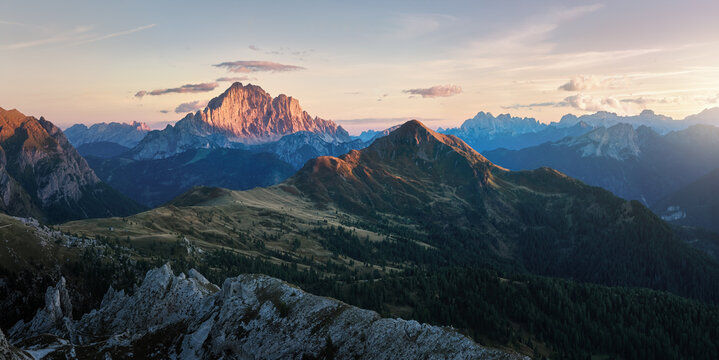 Panoramic mountain landscape with Monte Pelmo illuminated by warm sunset light above forested alpine ridges near the Cinque Torri area in the Italian Dolomites.