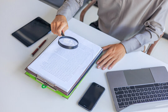 Professional closely inspecting a stack of organized documents and file folders on a desk with a magnifying glass, symbolizing a detailed financial audit, document review, or fraud investigation.