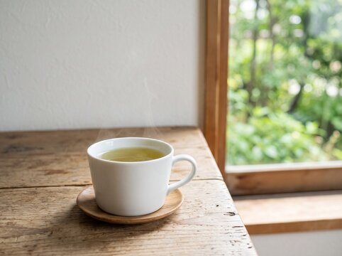 木のテーブルに置いた温かいお茶と窓辺の緑