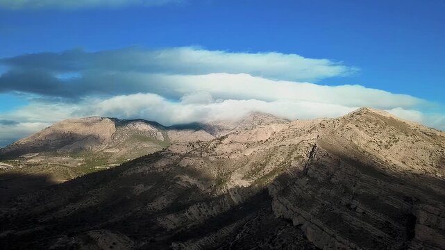 Panoramic view of rugged mountain peaks under a dramatic sky with soft rolling clouds at sunset