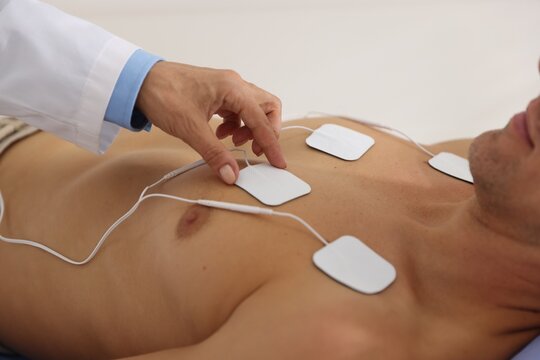 Doctor attaching ECG electrodes to patient's chest in clinic, closeup