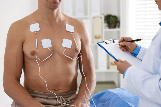 Doctor writing notes during patient's ECG test in clinic, closeup