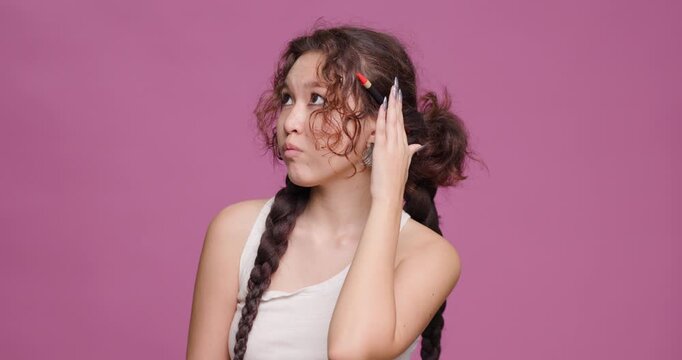 Young Kazakh woman with pen, displays contemplative expression against pink background