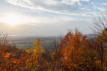 Fototapeta premium Autumn foliage overlooking valley landscape at sunset. Vibrant fall trees on hillside with distant river view. Champlain Lookout in Gatineau Park, Quebec, Canada.