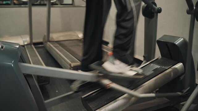 Low angle close up shot of feet in athletic sneakers stepping on elliptical cross trainer pedals during an indoor cardio exercise session in a modern gym.