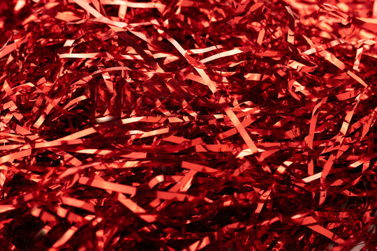 Gleaming red foil tinsel strips spread across surface forming dazzling holiday texture with glossy ribbon reflections, dynamic shimmer, seasonal elegance