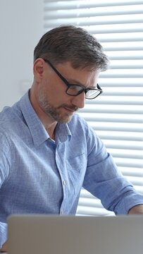 Businessman wearing blue sleek shirt, glasses, is thinking and concentrating while working at the desk in a bright, modern office, demonstrating professionalism and efficiency. Business people concept
