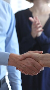 Business executives shaking hands during a successful corporate meeting, finalizing an important deal while a colleague claps in approval, symbolizing strong teamwork and growing success