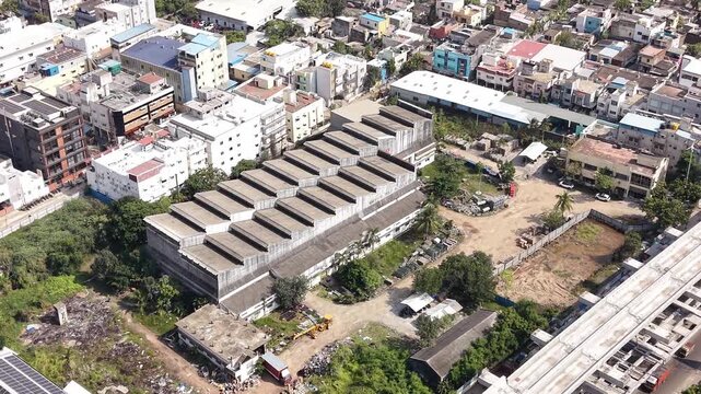 Aerial view of industrial warehouse with sawtooth roof surrounded by urban development and roads in Chennai, Tamil Nadu, India.