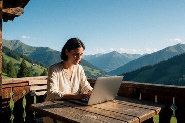 Fototapeta premium Young woman works on laptop computer on wooden balcony. Freelancer uses notebook at outdoor terrace with scenic mountain landscape view. Person focuses on remote job enjoying sunny summer day in