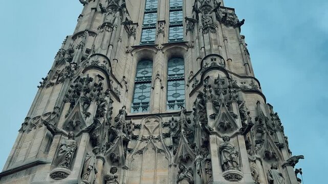 A smooth tilt shot revealing the intricate Flamboyant Gothic architecture and ornate carved stonework of the historic Tour Saint Jacques against an overcast sky in central Paris, France.

