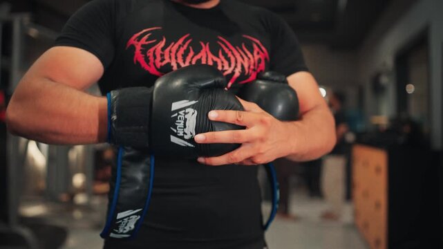 Close up detail shot of a male boxer adjusting velcro wrist straps on Venum boxing gloves preparing for an intense martial arts or combat sports training session.