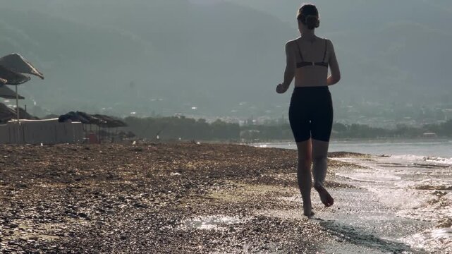 A video of an eight year old female one eyed pitbull running together with her thirty year old female owner on a sunny morning sandy beach in warm golden sunlight.
