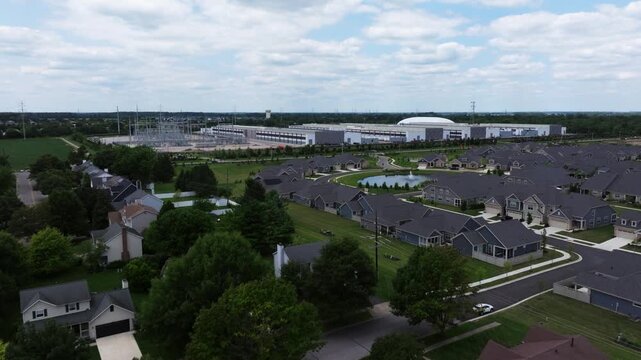 Aerial view of a large data center facility situated adjacent to a suburban residential neighborhood with houses and green trees in the United States.