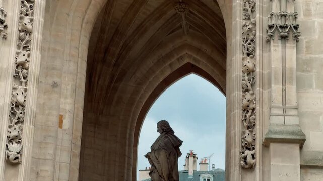 A smooth tilt shot revealing the intricate Flamboyant Gothic architecture and ornate carved stonework of the historic Tour Saint Jacques against an overcast sky in central Paris, France.

