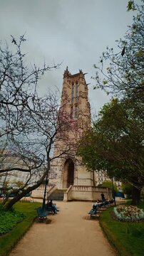A smooth tilt shot revealing the intricate Flamboyant Gothic architecture and ornate carved stonework of the historic Tour Saint Jacques against an overcast sky in central Paris, France.

