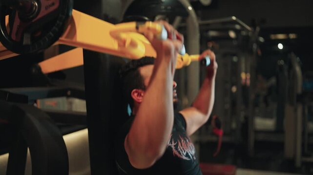 Low angle close up shot of a man's hands gripping and pushing handles on a plate-loaded shoulder press machine during a gym workout.