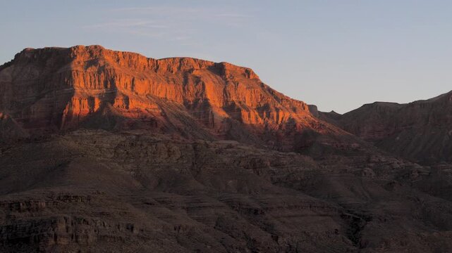 Sunlight slowly disappearing from rugged rocks canyon peaks during serene sunset, illuminating grand rocky landscape with warm and golden glow against a clear twilight sky