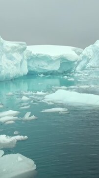 Vertical Video of Floating Ice Pieces Spread Across Turquoise Water. Broken white ice spreads across blue-green water, showing varied frozen shapes, texture and gentle ripples.