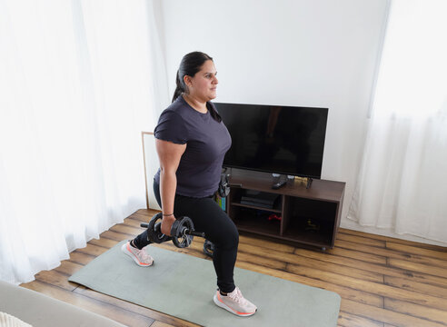 Mujer de talla grande haciendo zancada inversa con mancuernas en casa