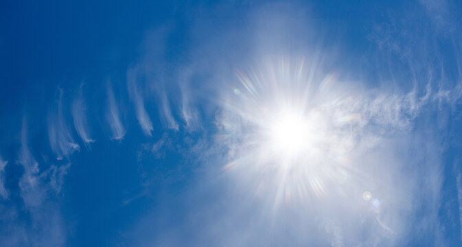 Bright sun shining in clear blue sky with cirrus clouds background