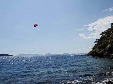 ​Slow motion view of parasailing over serene turquoise sea with gentle waves and rocky pine cliffs in Fethiye Turkey