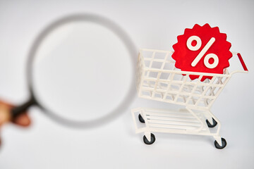 Magnifying glass examining a shopping cart with percentage symbol for discount research and price comparison isolated on white background  © kaliel